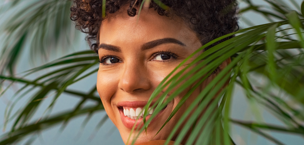 woman smiles among palm fronds with summery skin