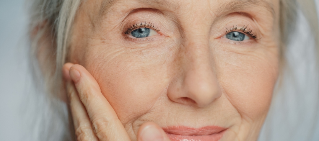 an elderly woman looks at the camera and gently touches her face