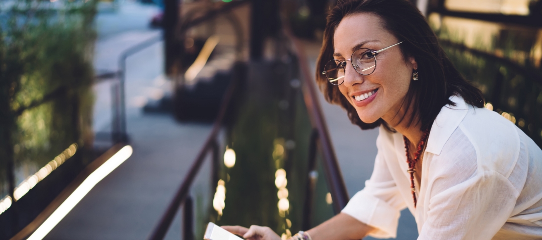 a slim woman in her 30s leans over a handrail smiling