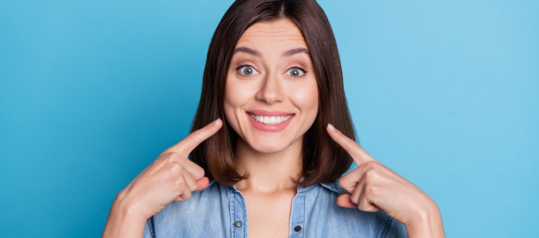 woman pointing at her smile with light blue background